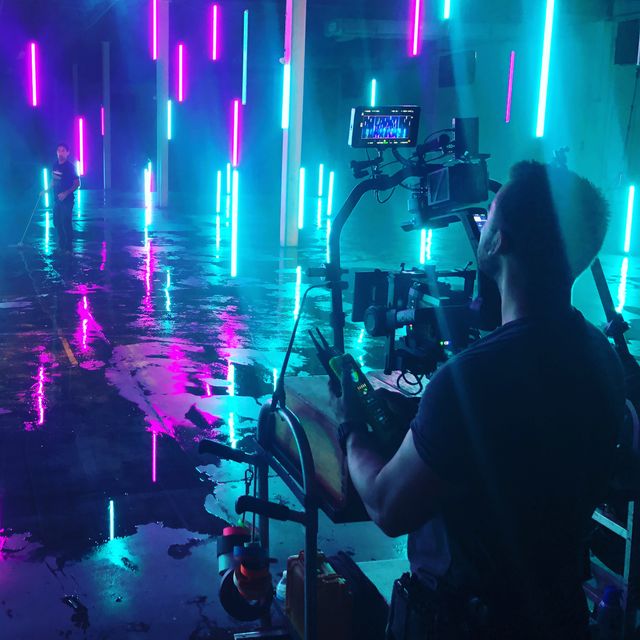 Filmmaker captures neon lights scene in vibrant studio with reflective floor and colorful illumination.