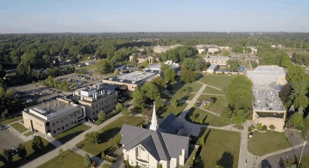 Aerial view of a lush college campus with pathways, buildings, and trees under a clear blue sky.