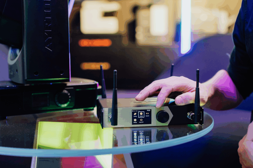 Person adjusting wireless device on glass table with colorful reflections in a tech setup.